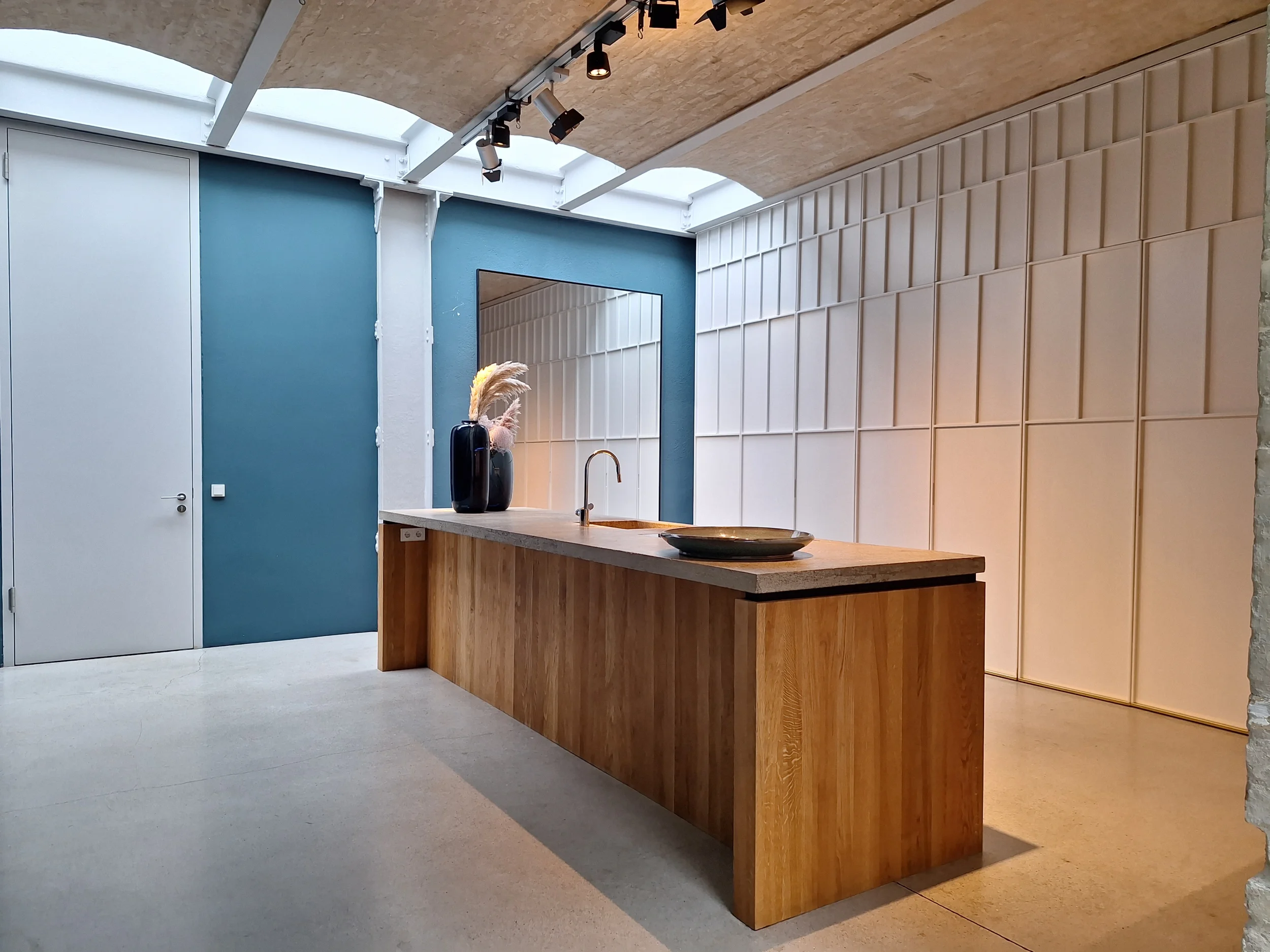Design-Wohnküche für Jorinde Voigt mit integriertem BORA Kochfeld auf einer Betonarbeitsplatte vor einer petrolblauen Wand mit großem Spiegel von STUDIOLIVIUS.
