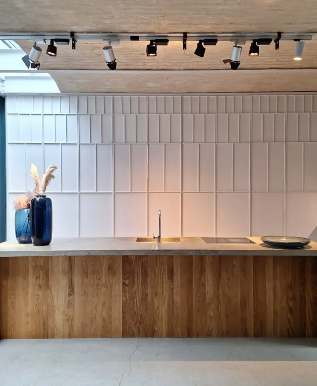 Offene Loft-Küche mit einer freistehenden Beton-Kücheninsel, integrierter Spüle und Sichtmauerwerk neben einer skulpturalen Schrankfront von STUDIOLIVIUS.