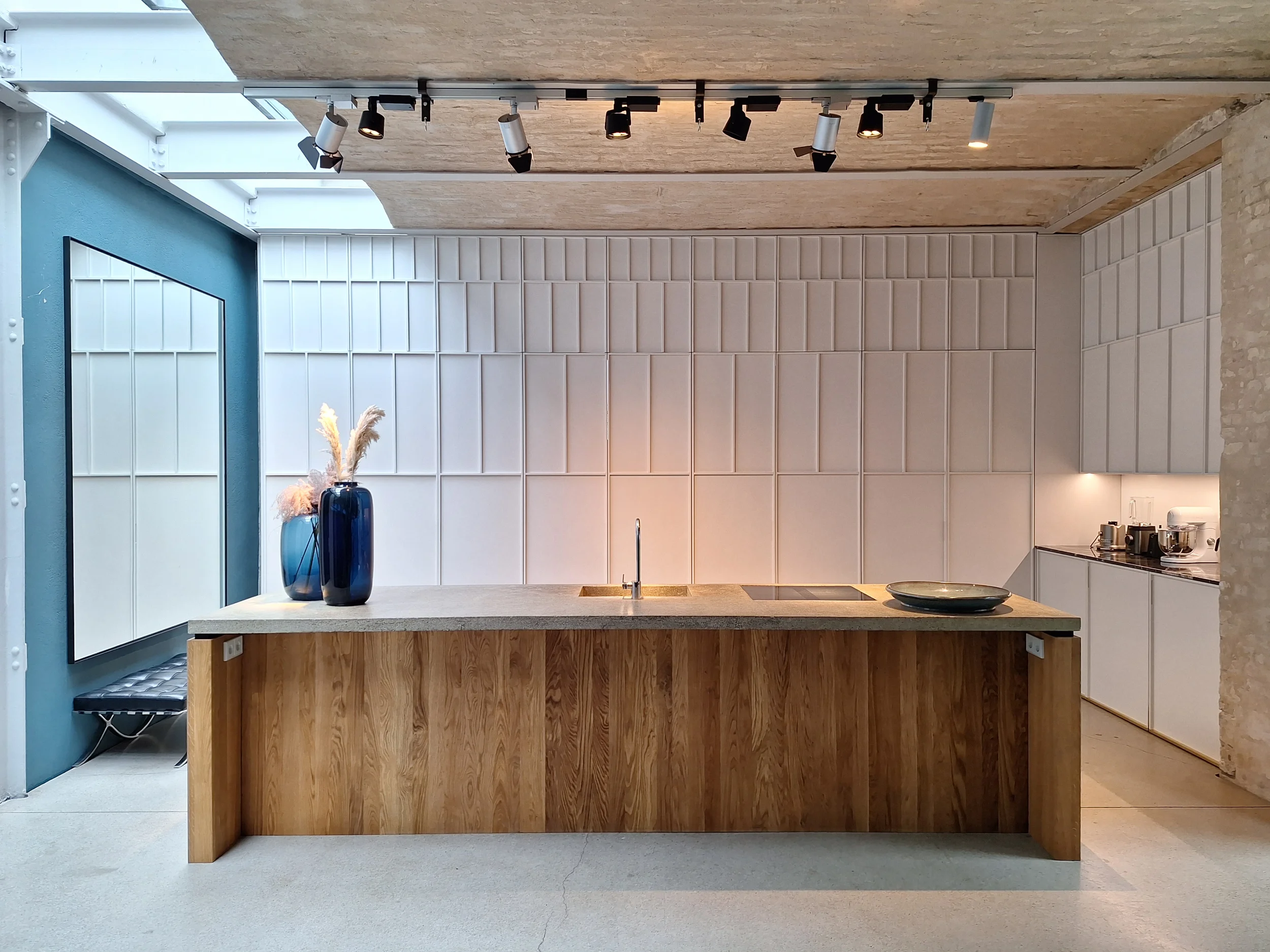 Offene Loft-Küche mit einer freistehenden Beton-Kücheninsel, integrierter Spüle und Sichtmauerwerk neben einer skulpturalen Schrankfront von STUDIOLIVIUS.