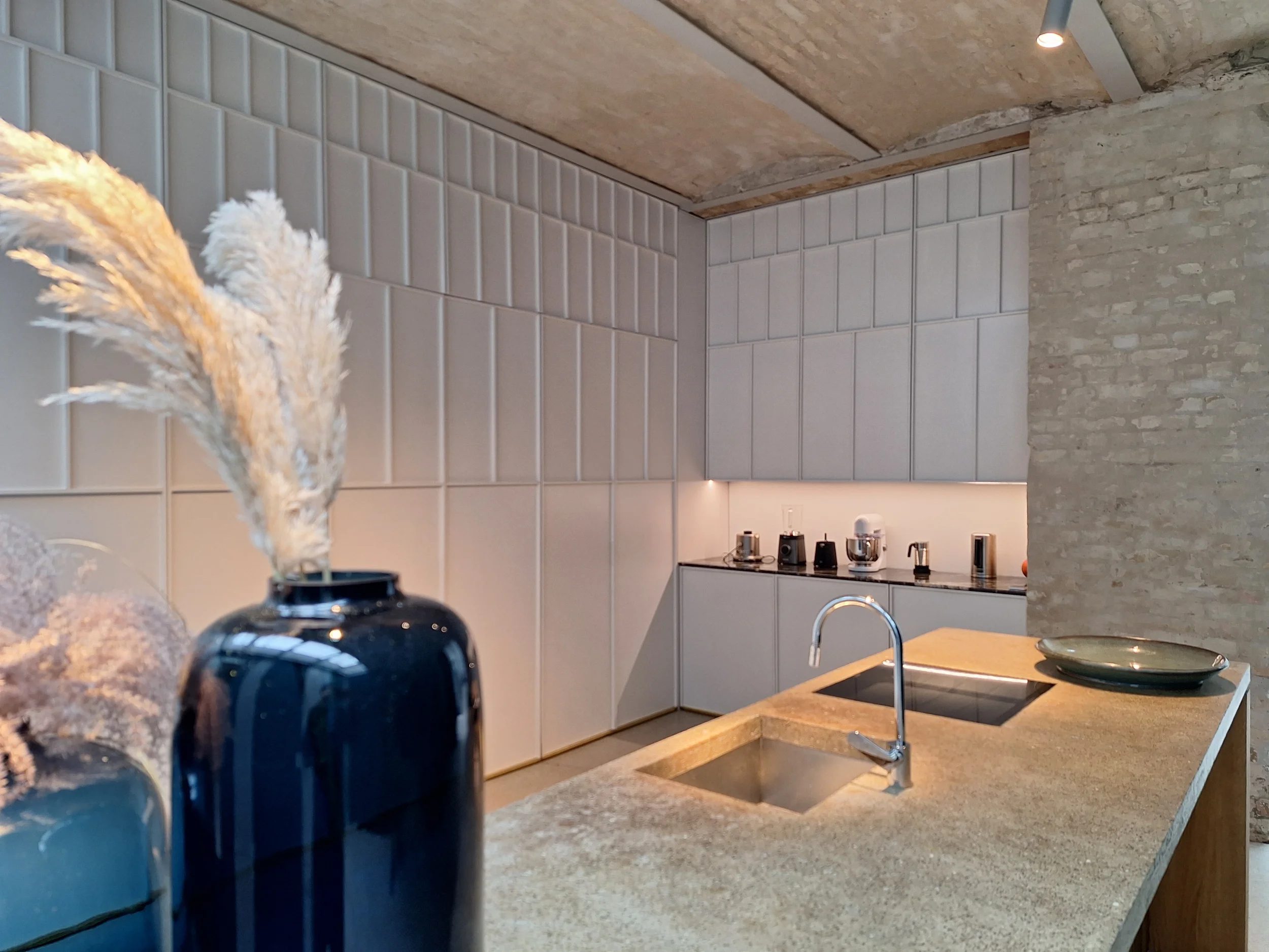 Moderne Wohnküche in einer Berliner Remise mit einer Kücheninsel aus Eiche und Beton sowie einer raumhohen, weißen Schrankwand im Goldenen Schnitt von STUDIOLIVIUS.