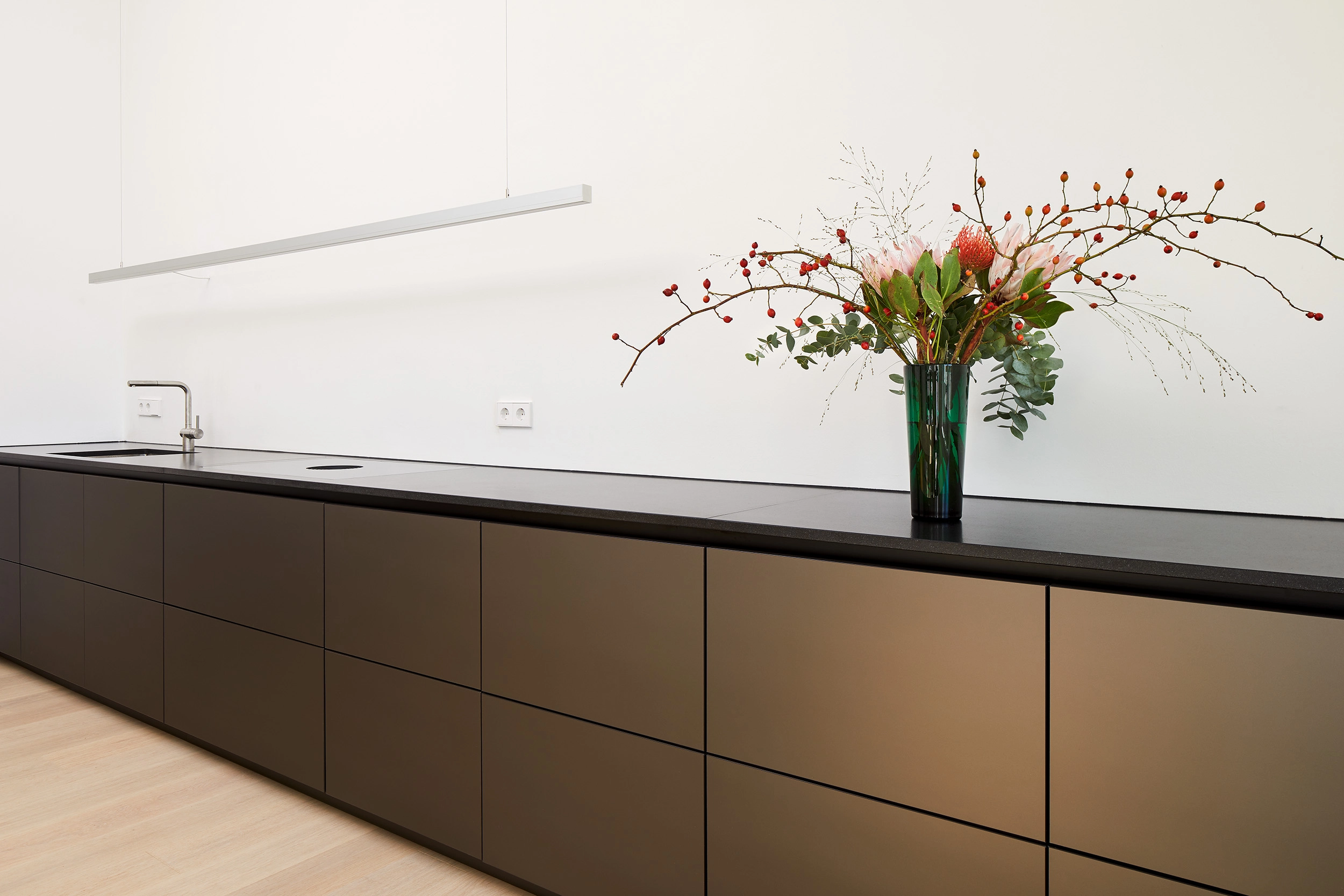minimalistische Einbauküchenzeile ohne Griffe mit bronzefarbenen Fronten und einer Arbeitsplatte aus Nero Assoluto Granit von STUDIOLIVUS