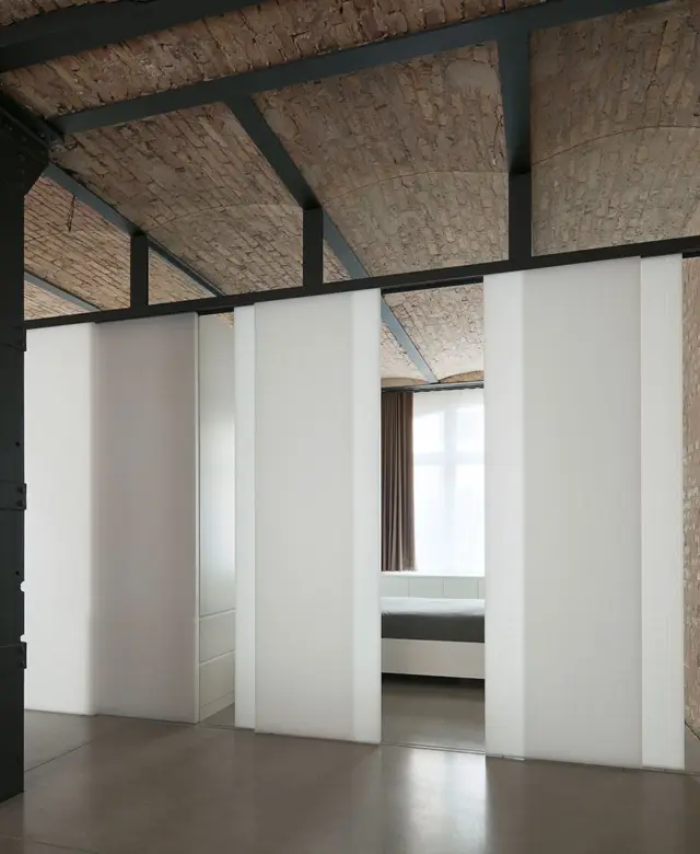 Raumhohe, transluzente Schiebetüren als modularer Raumteiler vor einer weißen Einbauschrankwand unter einer historischen Ziegel-Kappendecke von STUDIOLIVIUS Innenausbau.