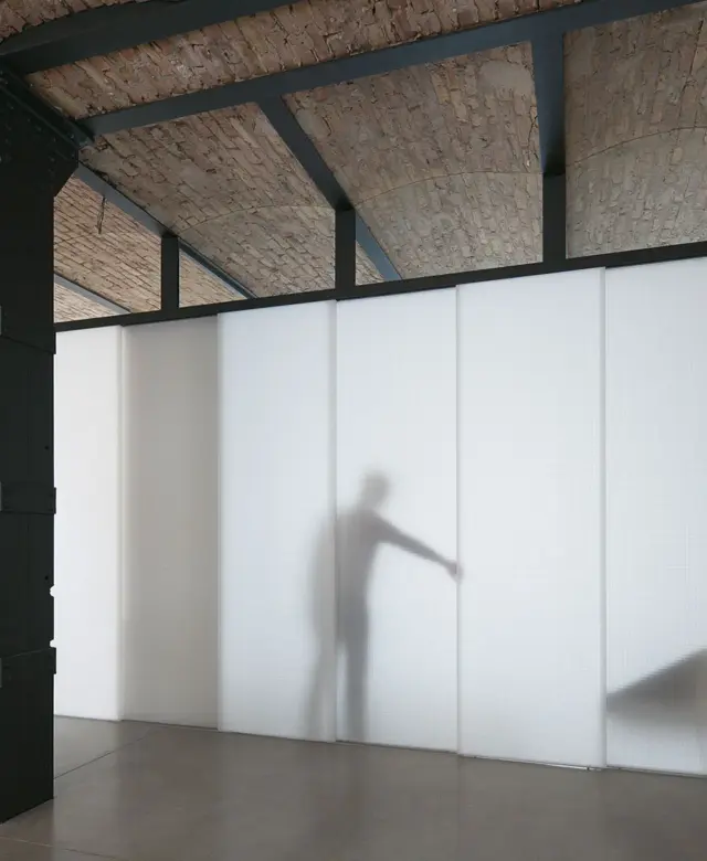 Geschlossenes, lichtdurchlässiges Schiebewandsystem aus strukturiertem Material vor Sichtziegelmauerwerk und geschliffenem Sichtestrich-Boden in einer Remise von STUDIOLIVIUS.