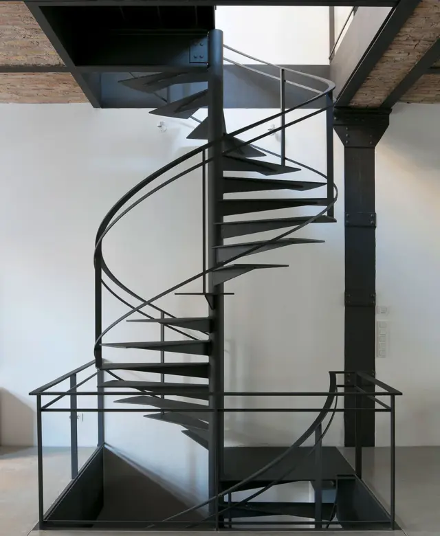 Filigrane, maßgefertigte Spindeltreppe aus anthrazitfarben lackiertem Stahl in einem Loft-Innenausbau mit Kappendecke und historischer Industriearchitektur von STUDIOLIVIUS.