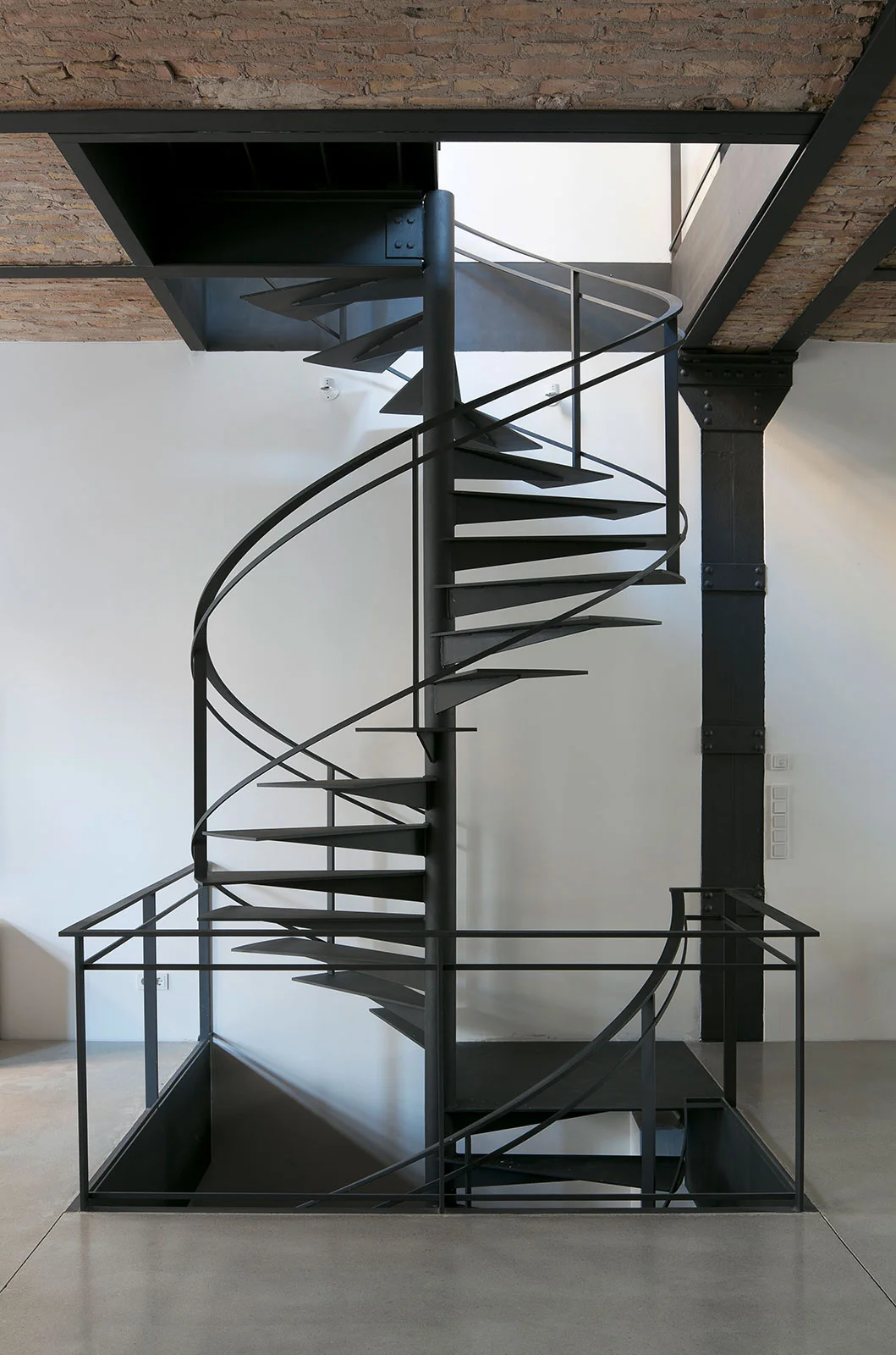 Filigrane, maßgefertigte Spindeltreppe aus anthrazitfarben lackiertem Stahl in einem Loft-Innenausbau mit Kappendecke und historischer Industriearchitektur von STUDIOLIVIUS.
