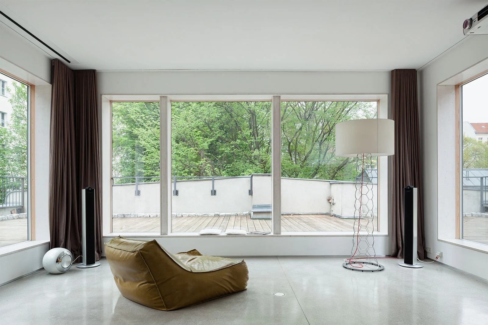 Lichtdurchfluteter Wohnbereich in einer Remise mit raumhoher Fensterfront zur Holzterrasse, geschliffenem Betonboden und minimalistischem Interior Design von STUDIOLIVIUS Berlin.
