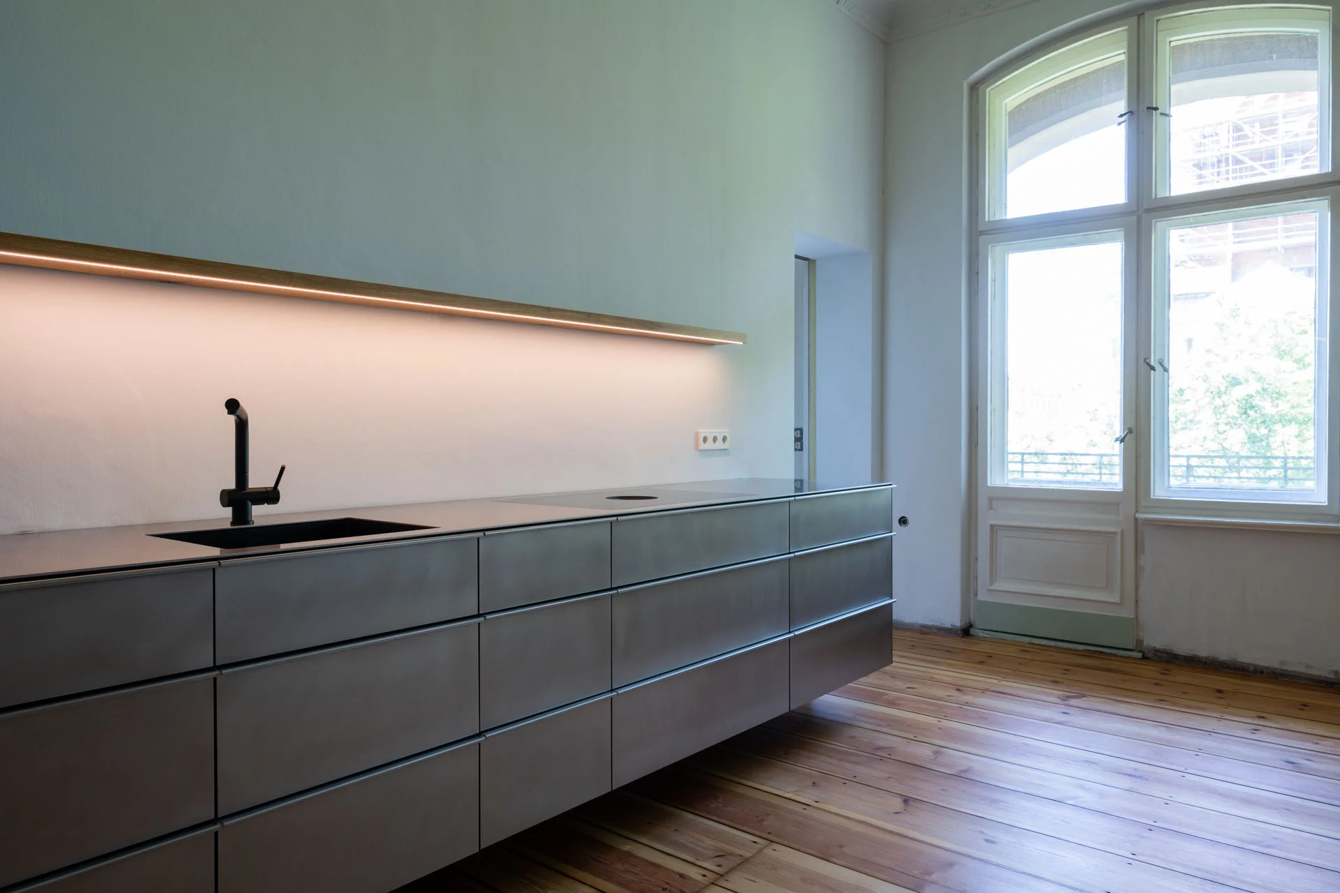 Raumansicht einer schwebenden Küche aus Edelstahl mit einem beleuchteten Regalbrett in einer Berliner Altbauwonung von STUDIOLIVIUS