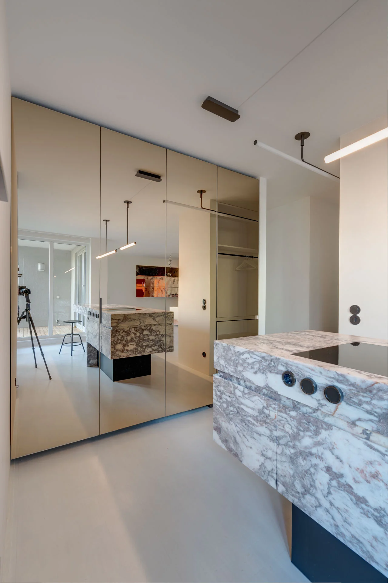 Einbauküche im modernen Loft mit grifflosen Fronten und einer raumöffnenden Rückwand aus bronziertem Spiegelglas.