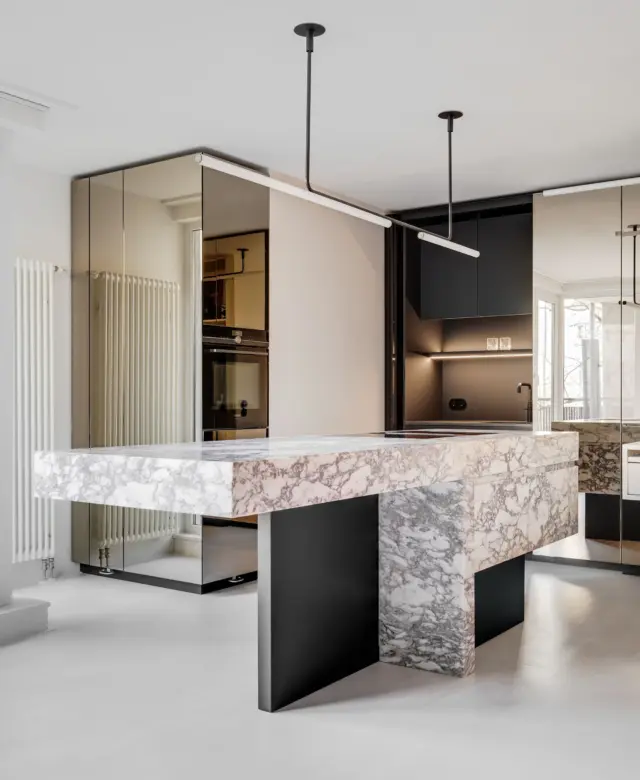 Offenes Küchendesign in Berlin-Mitte mit einem Monolithen aus Naturstein und einer reflektierenden Spiegel-Schrankwand.