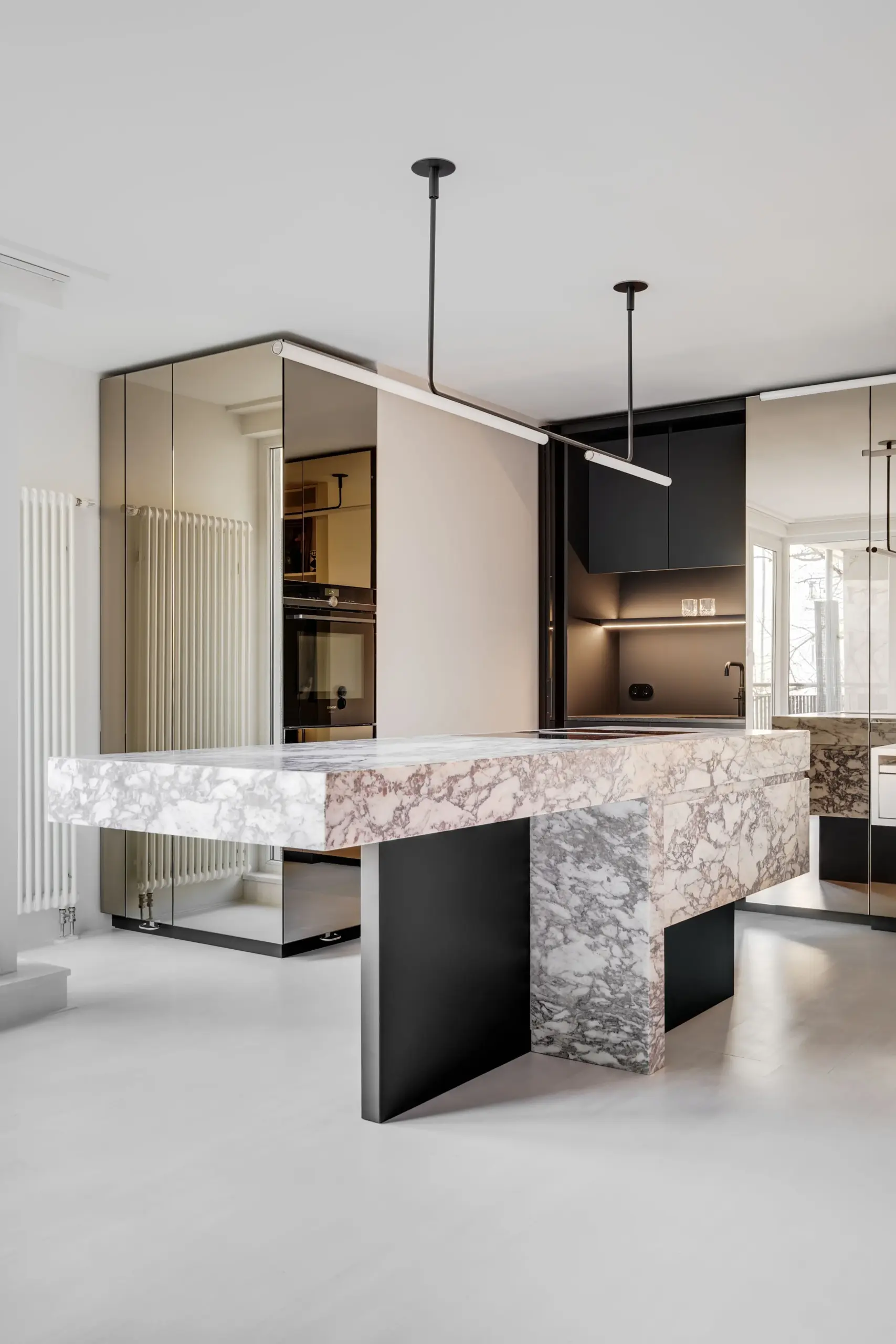 Offenes Küchendesign in Berlin-Mitte mit einem Monolithen aus Naturstein und einer reflektierenden Spiegel-Schrankwand.